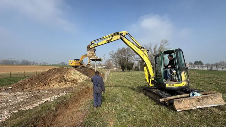 Escavatore cingolato che scava un fosso lungo un campo
