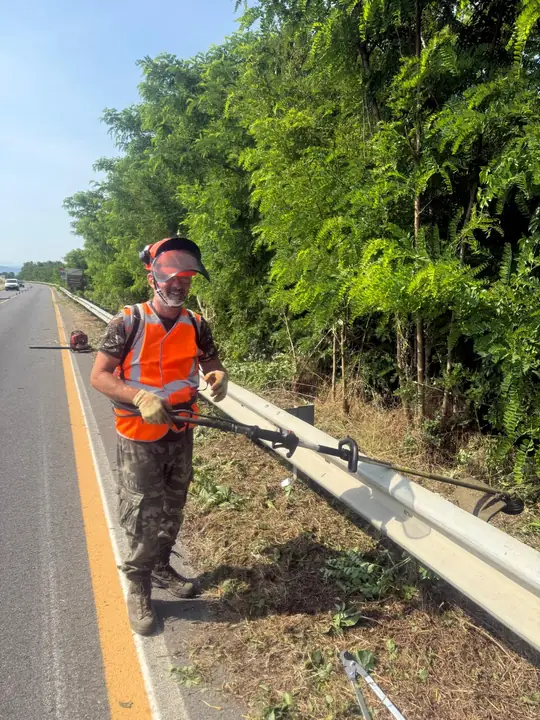 Operatore con decespugliatore durante lo sfalcio lungo una strada