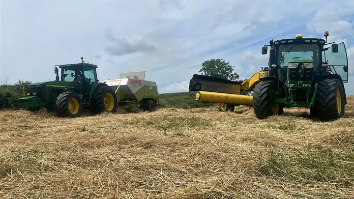 Trattori e pressa tra il fieno appena sfalciato